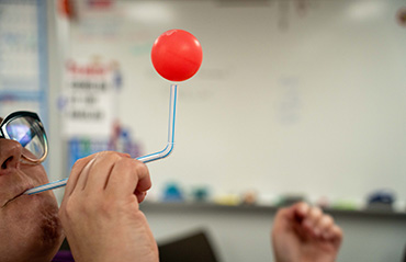 A person blow a ping pong using a straw