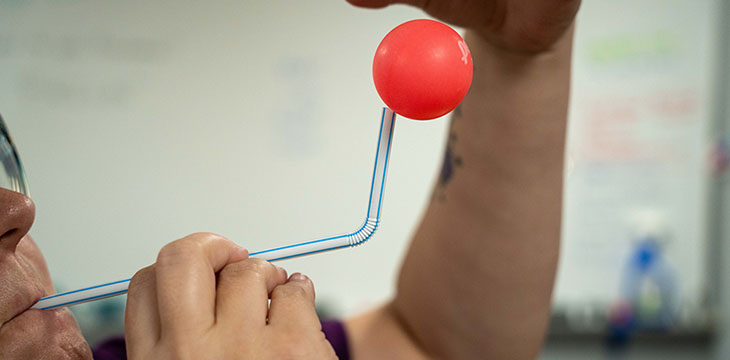 A person put a ping pong ball over a straw