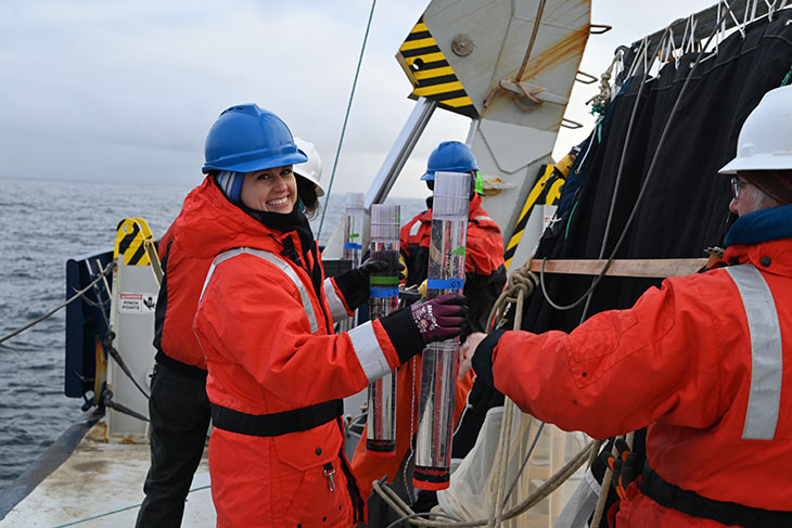 Lydia Babcock-Adams working with a sediment trap aboard the Research Vessel Roger Revelle. Scientists working on the deck of the boat must wear float coats and hardhats for safety.
